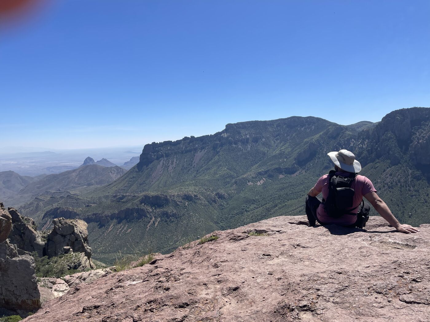 Jaabel sitting on a rock ledge overlooking a wide desert mountain range